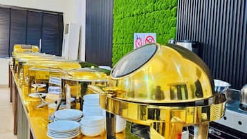 Disposição de buffet com diversos recipientes de comida e uma churrasqueira grande no centro.