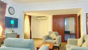 Un salon comprenant un canapé, des fauteuils, une table basse, un téléviseur et un appareil de climatisation.