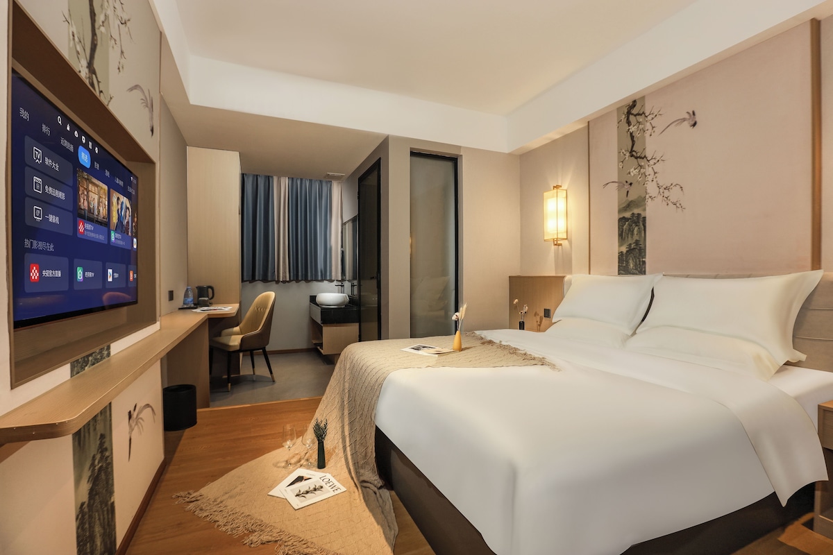 A hotel room with a bed, a desk with a computer, a TV, and a bathroom visible through an open door.