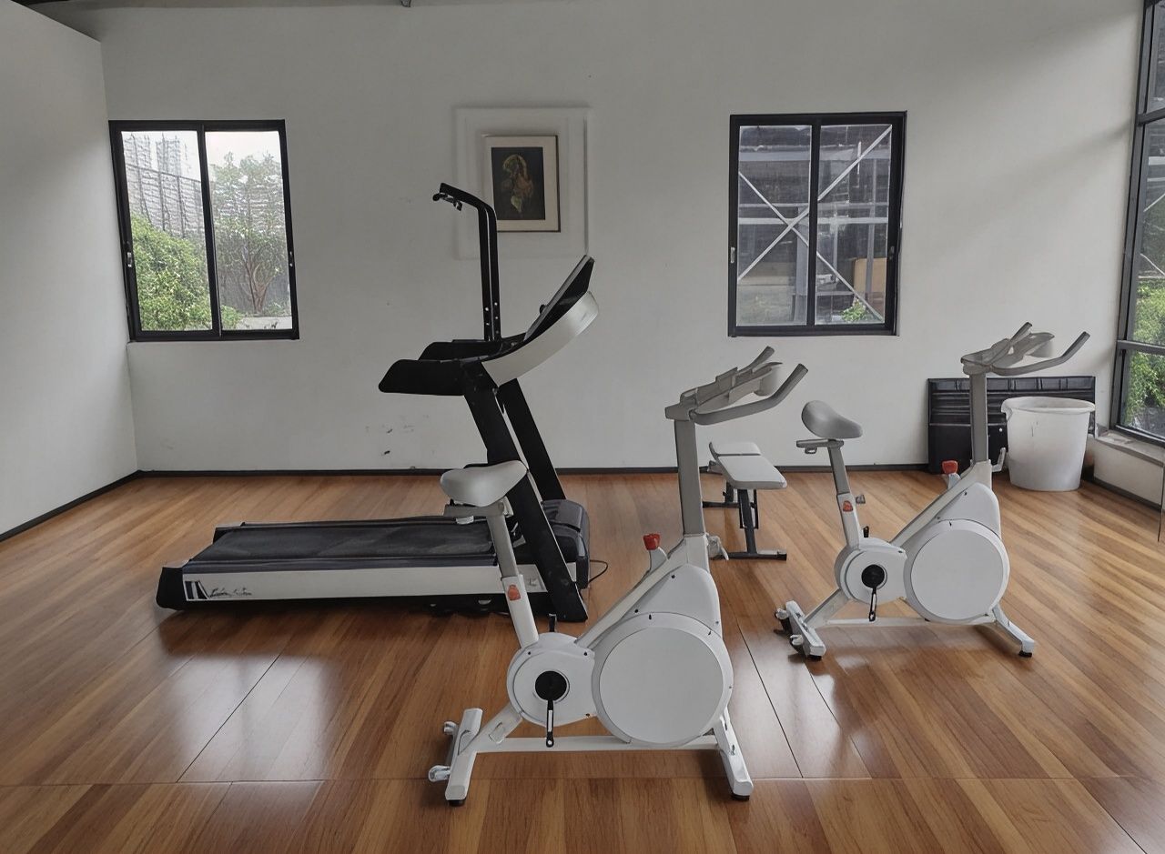 Un gimnasio con equipo de ejercicio, suelo de madera y ventanas con vistas.