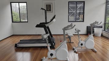 Un gimnasio con equipo de ejercicio, suelo de madera y ventanas con vistas.