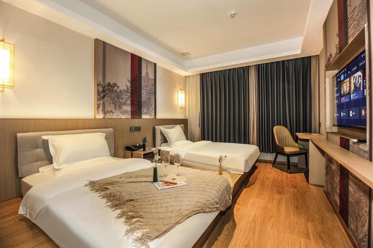 A hotel room with two beds, a desk, a television, and a large painting on the wall.