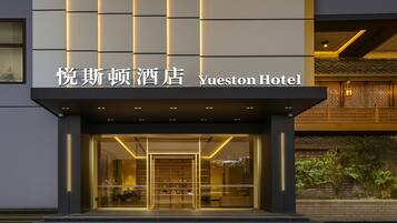 The exterior of Yueston Hotel with a modern facade, illuminated entrance, and traditional architectural elements.