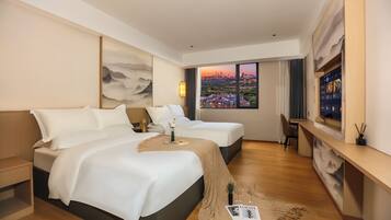 A hotel room with two beds, a desk, a large window with a city view, and a painting on the wall.