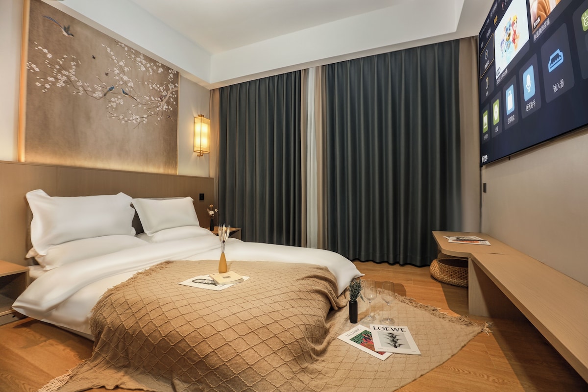 A hotel room with a bed, a bedside table, a lamp, a TV, and a wall with a decorative piece.