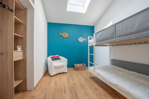 Ein kleines Zimmer mit Etagenbett, einem kleinen weißen Stuhl, einem Holzschrank und einer blauen Akzentwand.