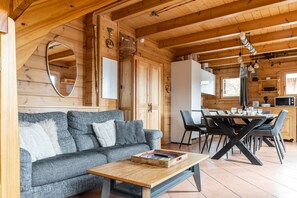 A wooden interior with a sofa, dining table, chairs, and a kitchen area.