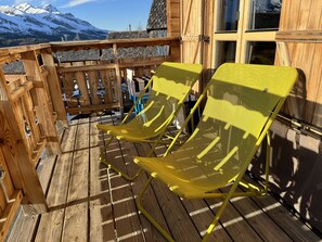 En træterrasse med to gule stole, et træhegn og udsigt til et bjerg.