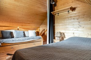 Quarto acolhedor de cabana de madeira, com uma cama, um banco com almofadas, um abajur e uma janela.
