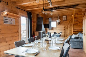 Interior em madeira com uma mesa de jantar posta para quatro pessoas, um sofá e uma lareira.