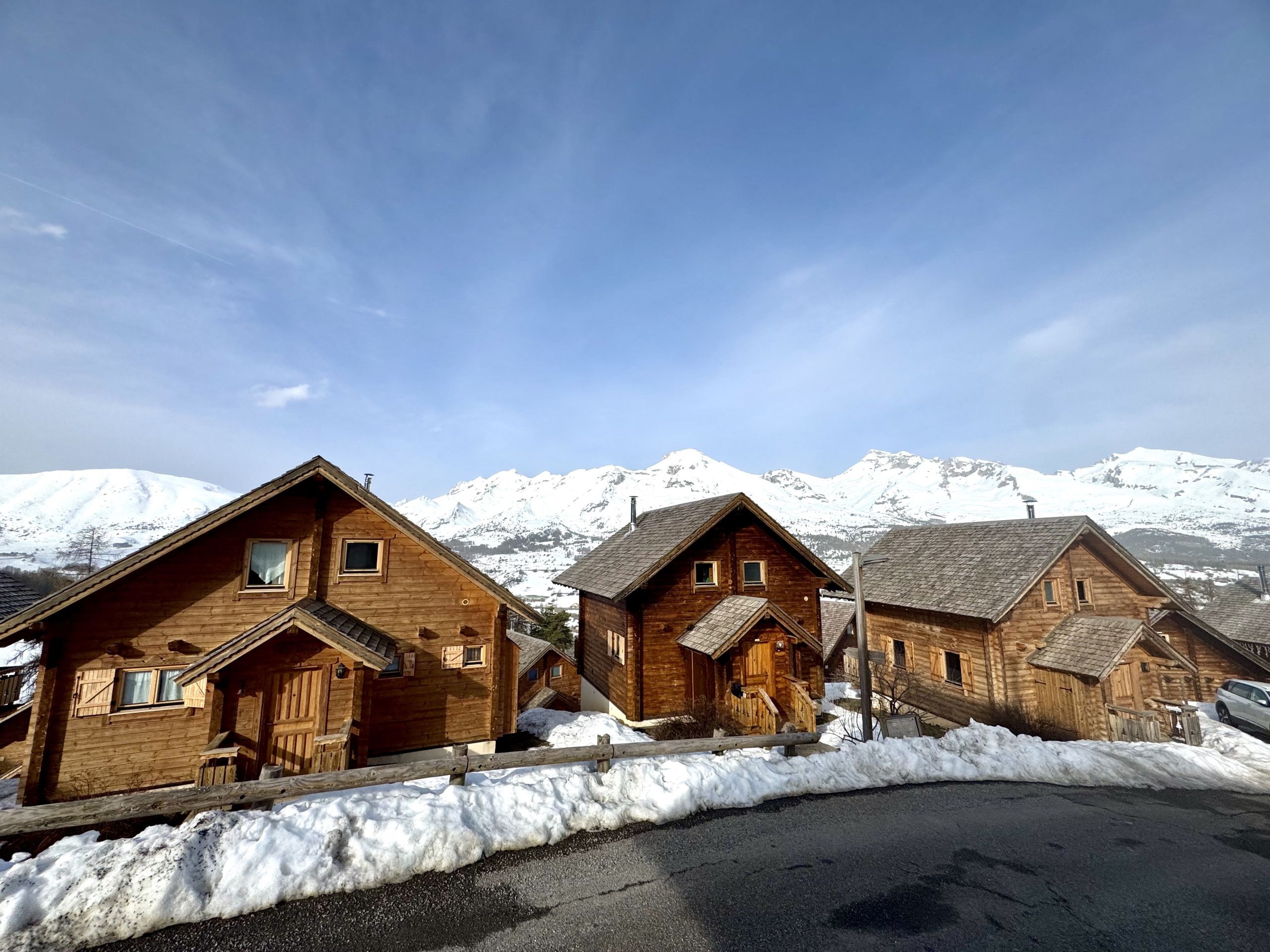 A row of wooden cabins with a snowy mountain backdrop.