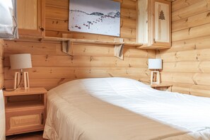 Ein schlichtes Schlafzimmer im Chalet-Stil mit einem Bett, Nachttischlampen, einem Beistelltisch und einem an der Wand hängenden Bild.