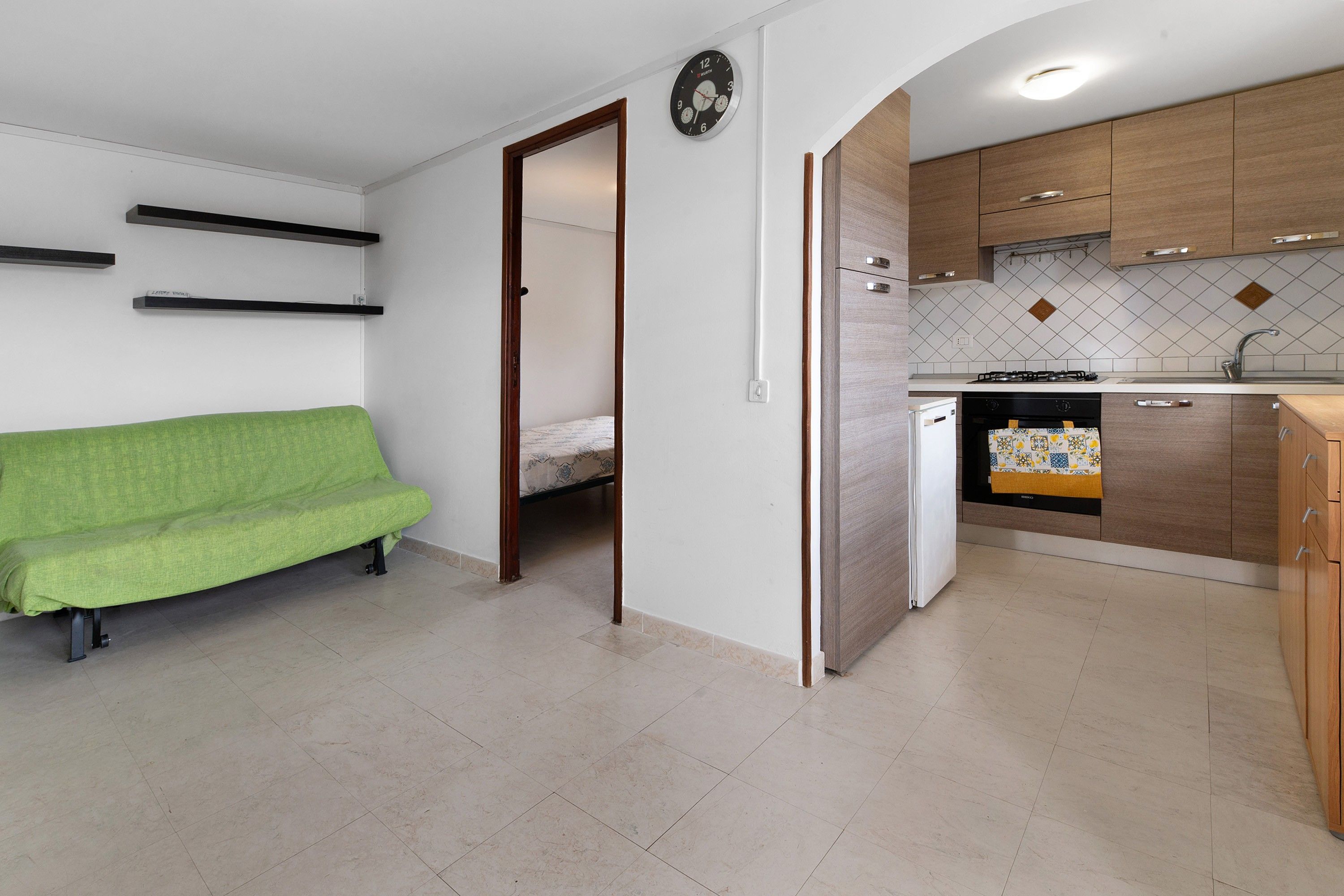 A compact living space with a kitchenette, a green sofa, and a bed in the adjacent room.