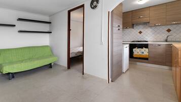 A compact living space with a kitchenette, a green sofa, and a bed in the adjacent room.