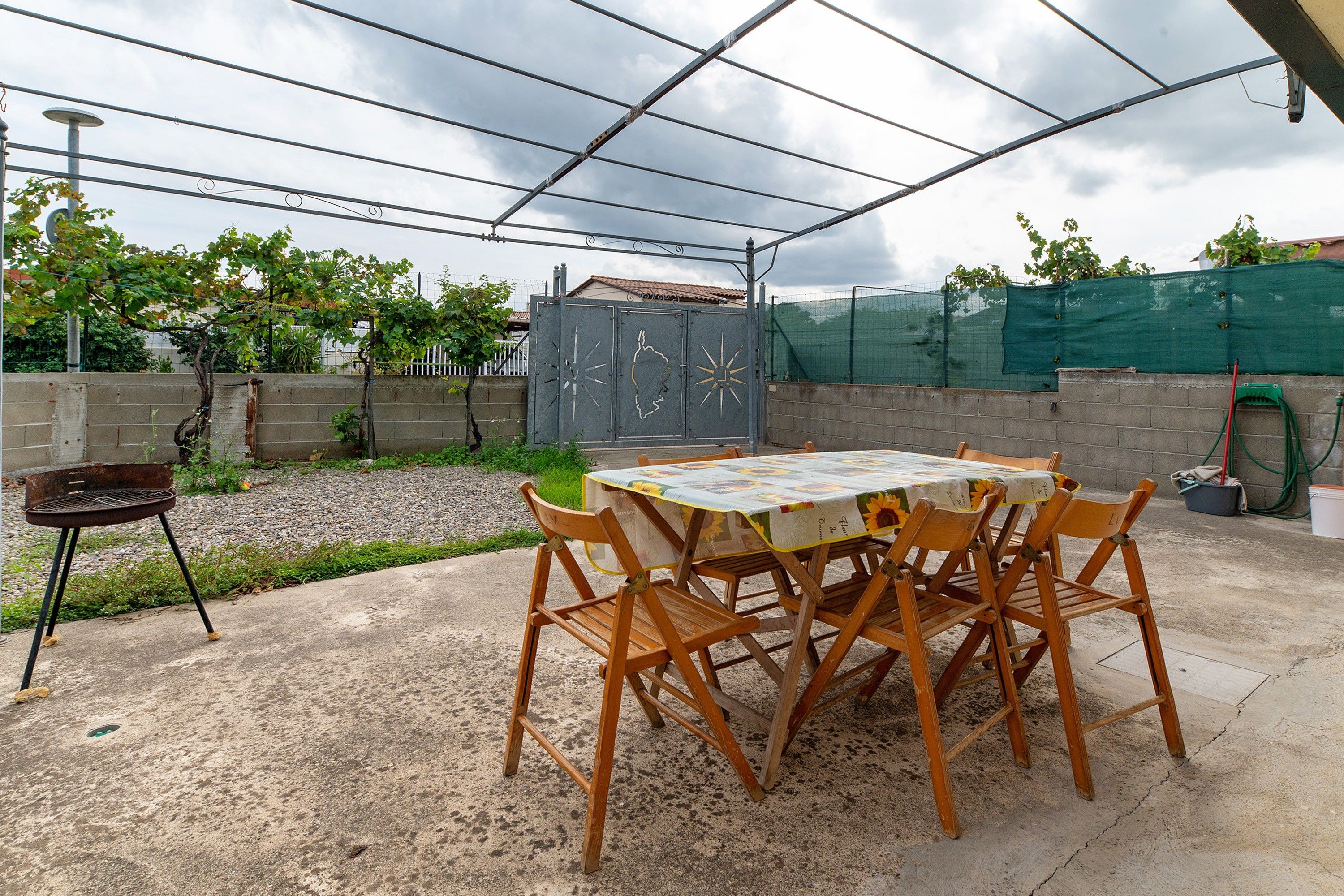 An outdoor patio with a table and chairs, a barbecue grill, and a fenced garden area.