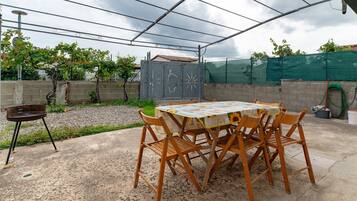 An outdoor patio with a table and chairs, a barbecue grill, and a fenced garden area.