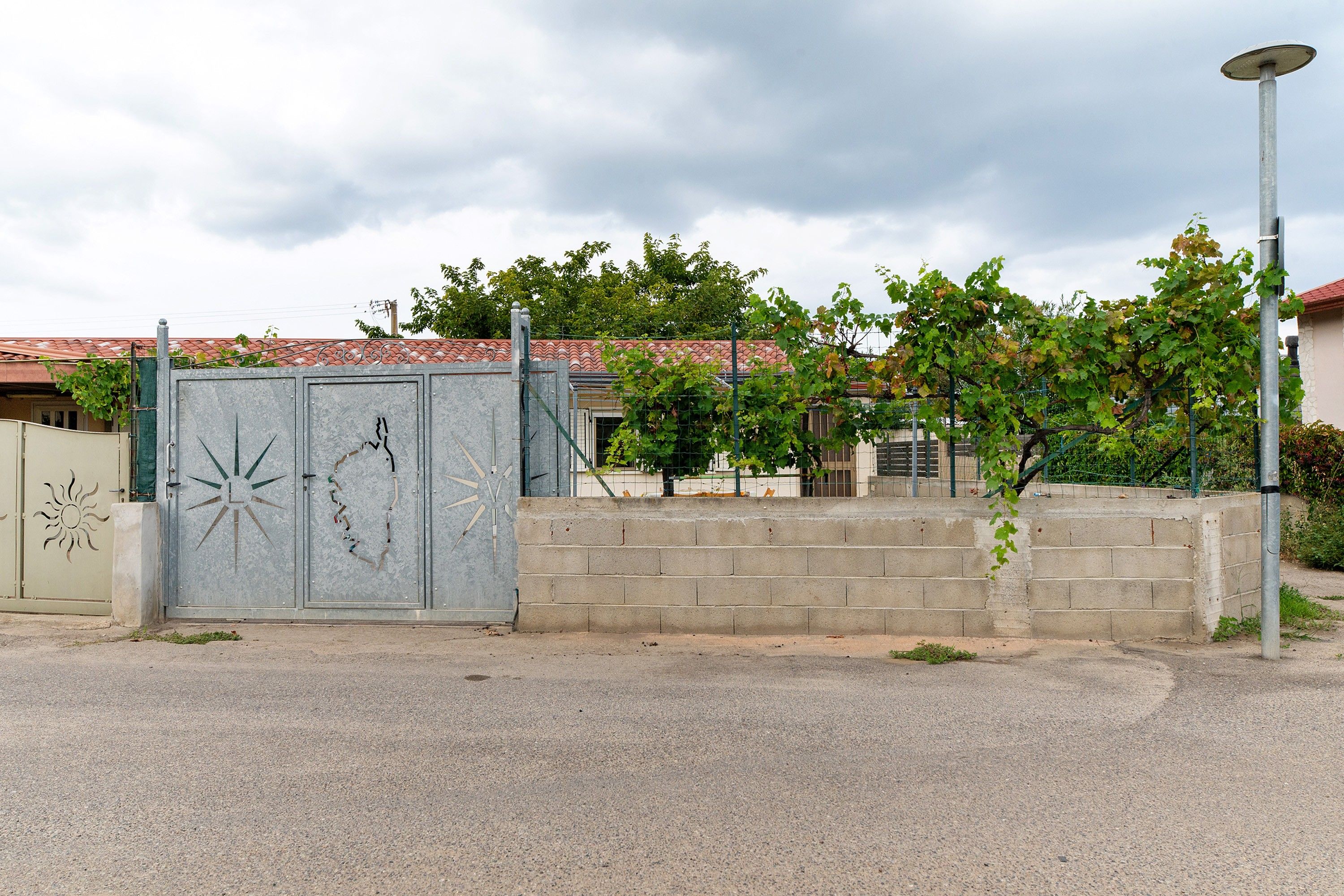 A gated entrance with a metal gate featuring decorative sunburst patterns, a concrete wall, and a street lamp.