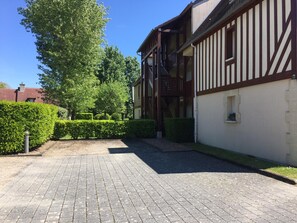 A courtyard with a paved walkway, a building with timber framing, and a large tree. - Holiday Home '2 Pièces À Deauville Avec Piscine' with Wi-Fi (Deauville)