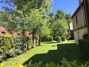 A well-maintained garden with a lawn, trees, and a building with a sloped roof. - Holiday Home '2 Pièces À Deauville Avec Piscine' with Wi-Fi (Deauville)