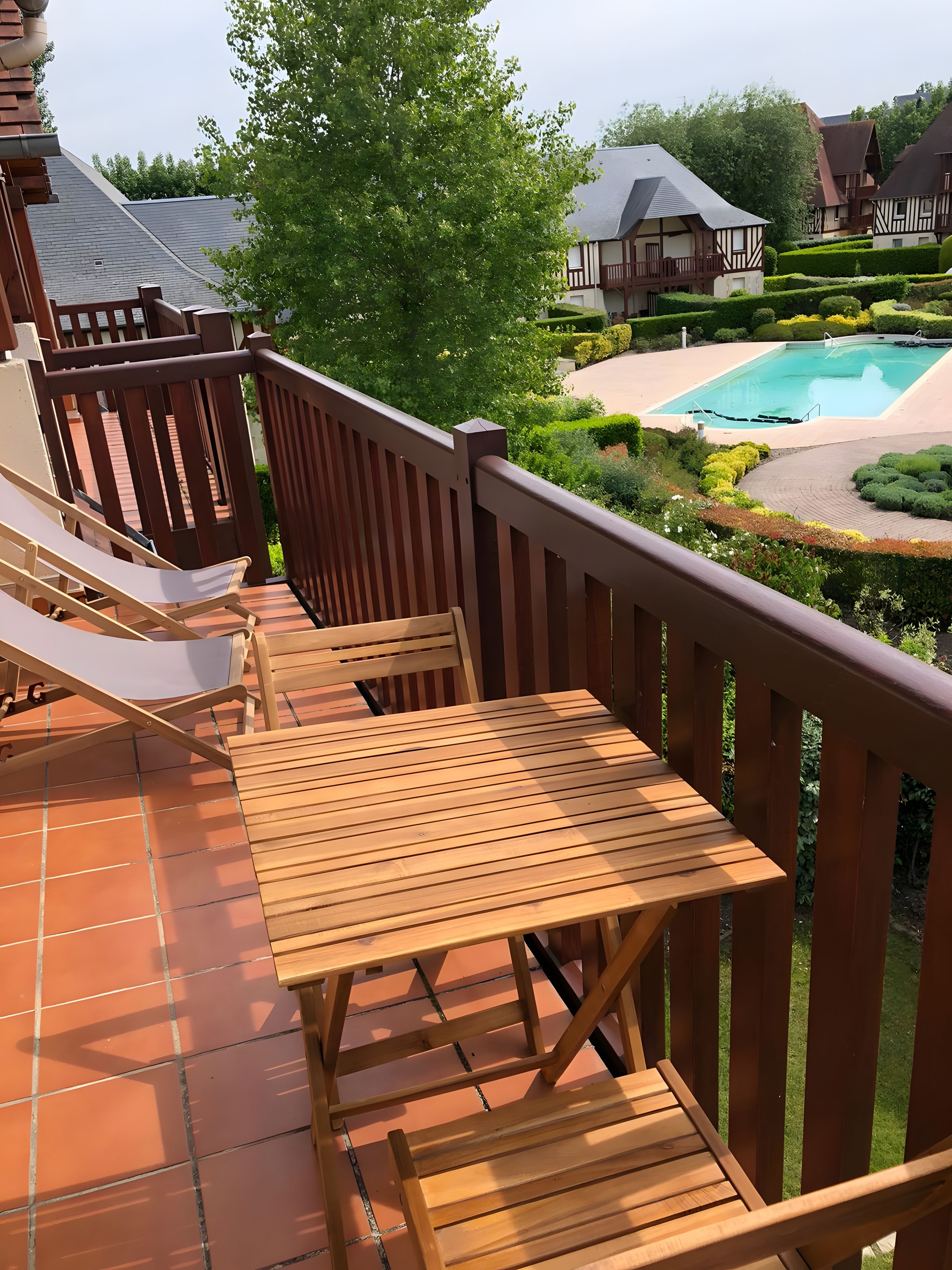 A wooden deck with outdoor seating and a view of a swimming pool.