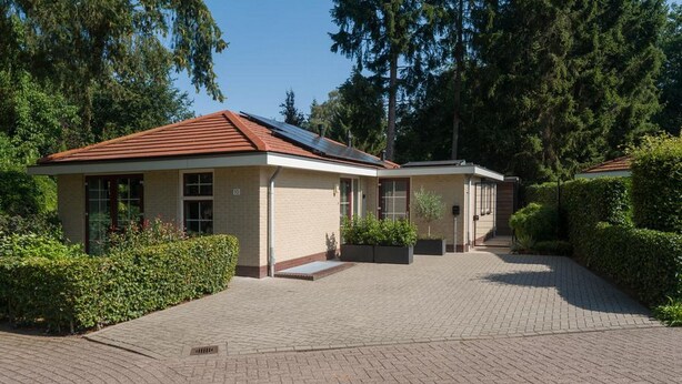En bygning med to etager, rødt tag, store vinduer og en belagt indkørsel.