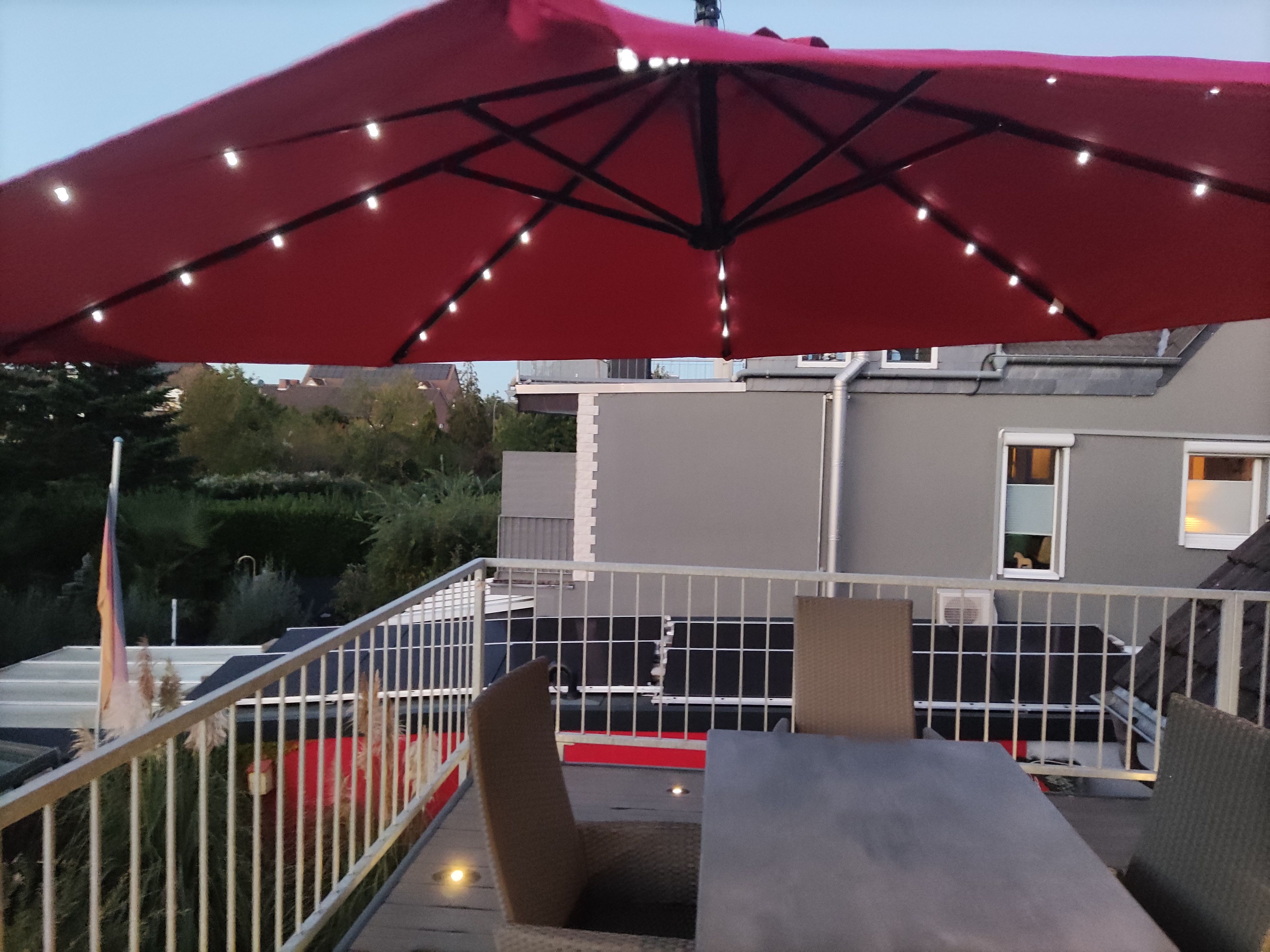 An outdoor patio with a red umbrella, a white railing, and a table with chairs.