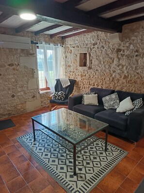 A living room with a stone wall, a sofa with patterned cushions, a glass coffee table, and a patterned rug. - La Maison du Bonheur 20 -seat (Plassac)