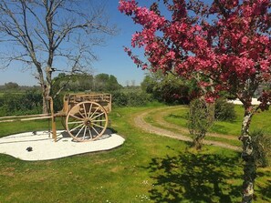 Un chariot en bois rustique, agrémenté d’une enseigne, est entouré d’une zone recouverte de gravier, avec de l’herbe et des arbres.