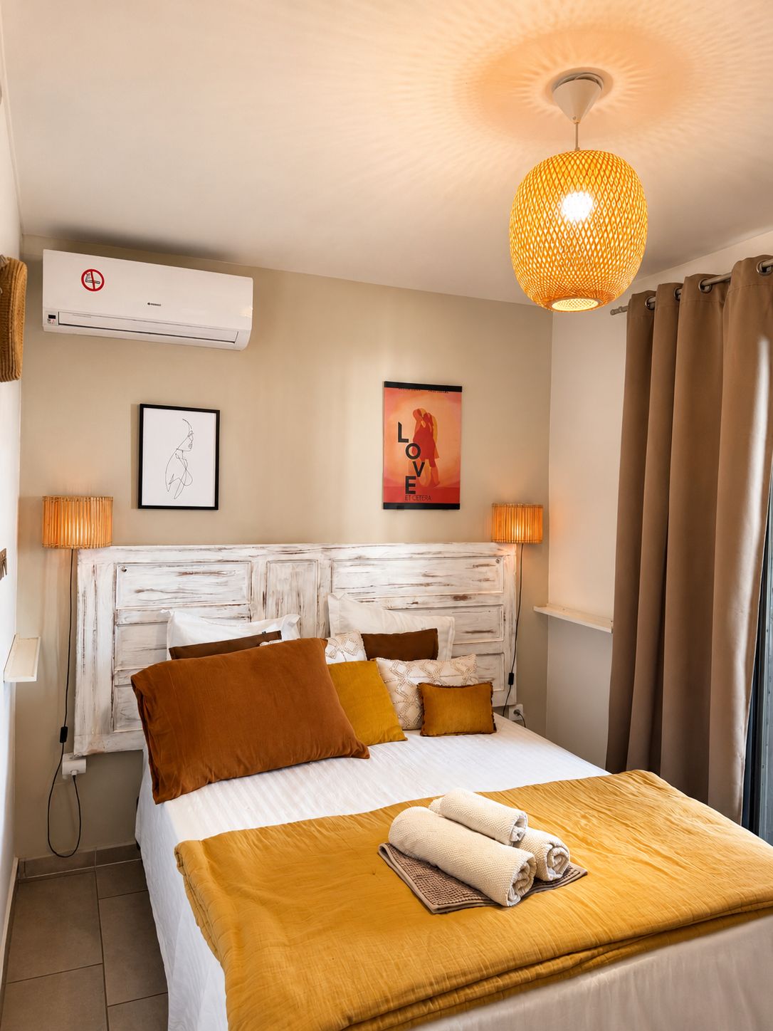 Habitación de hotel con cama, aire acondicionado de pared, un cartel y una lámpara colgante.