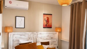 A hotel room with a bed, a wall-mounted air conditioner, a poster, and a hanging light fixture. - Côté Plage (Saint-Paul)