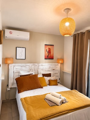 Habitación de hotel con cama, aire acondicionado de pared, un cartel y una lámpara colgante.