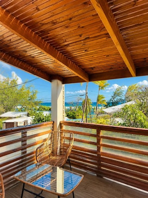 A covered outdoor seating area with a view of the ocean and palm trees.