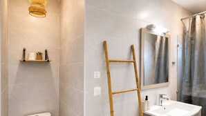 A bathroom with a toilet, a sink, a mirror, a shower curtain, and a wooden ladder. - Côté Plage (Saint-Paul)