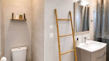 Un baño con inodoro, lavamanos, espejo, cortina de ducha y una escalera de madera.