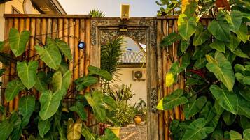 Um portão de madeira com arco decorativo, rodeado por plantas verdes exuberantes.