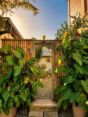 Una verja de madera con un arco decorativo, rodeada de abundante vegetación.