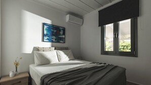 A bedroom with a bed, a nightstand, a wall-mounted air conditioner, a window with blinds, and a painting on the wall. - Binios Villa - private pool, walking distance from the Beach (Ano Vasilikos)