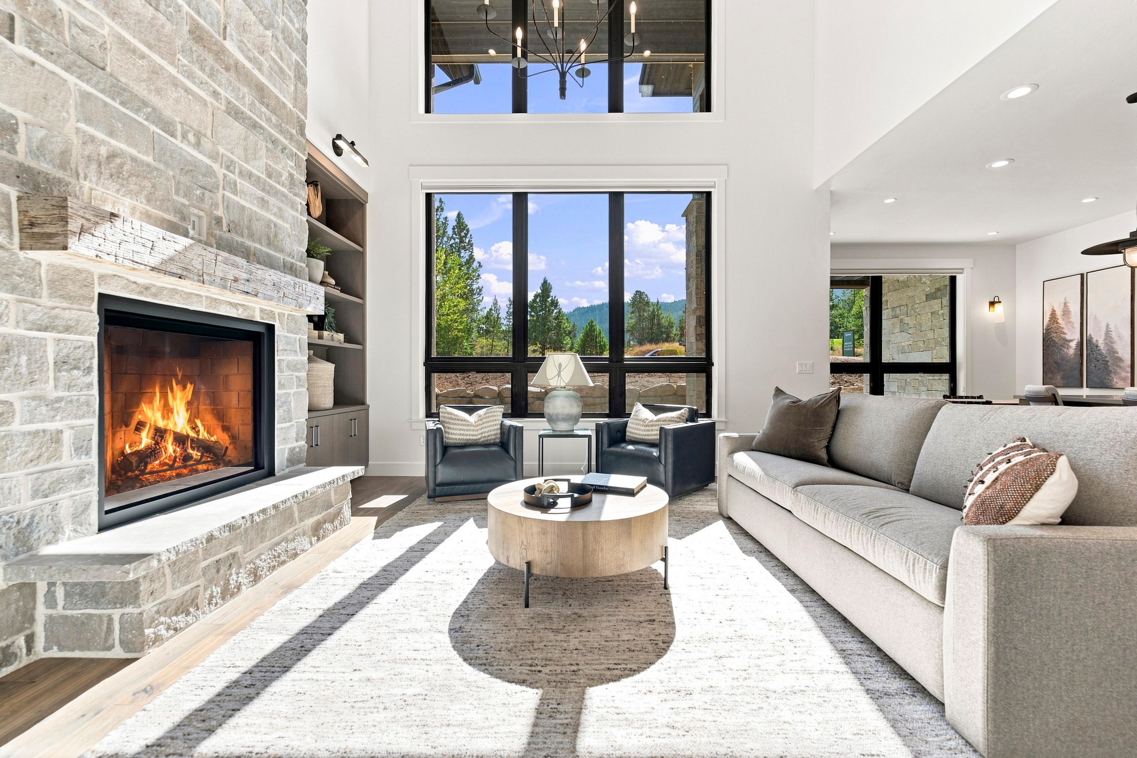 A modern living room with a stone fireplace, a large window with a view of trees, a sofa, and a coffee table.