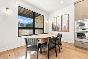 A modern kitchen with a large window, a dining table with chairs, and a built-in oven. - Everpine Haus | Exclusive Tamarack Perks (Tamarack)