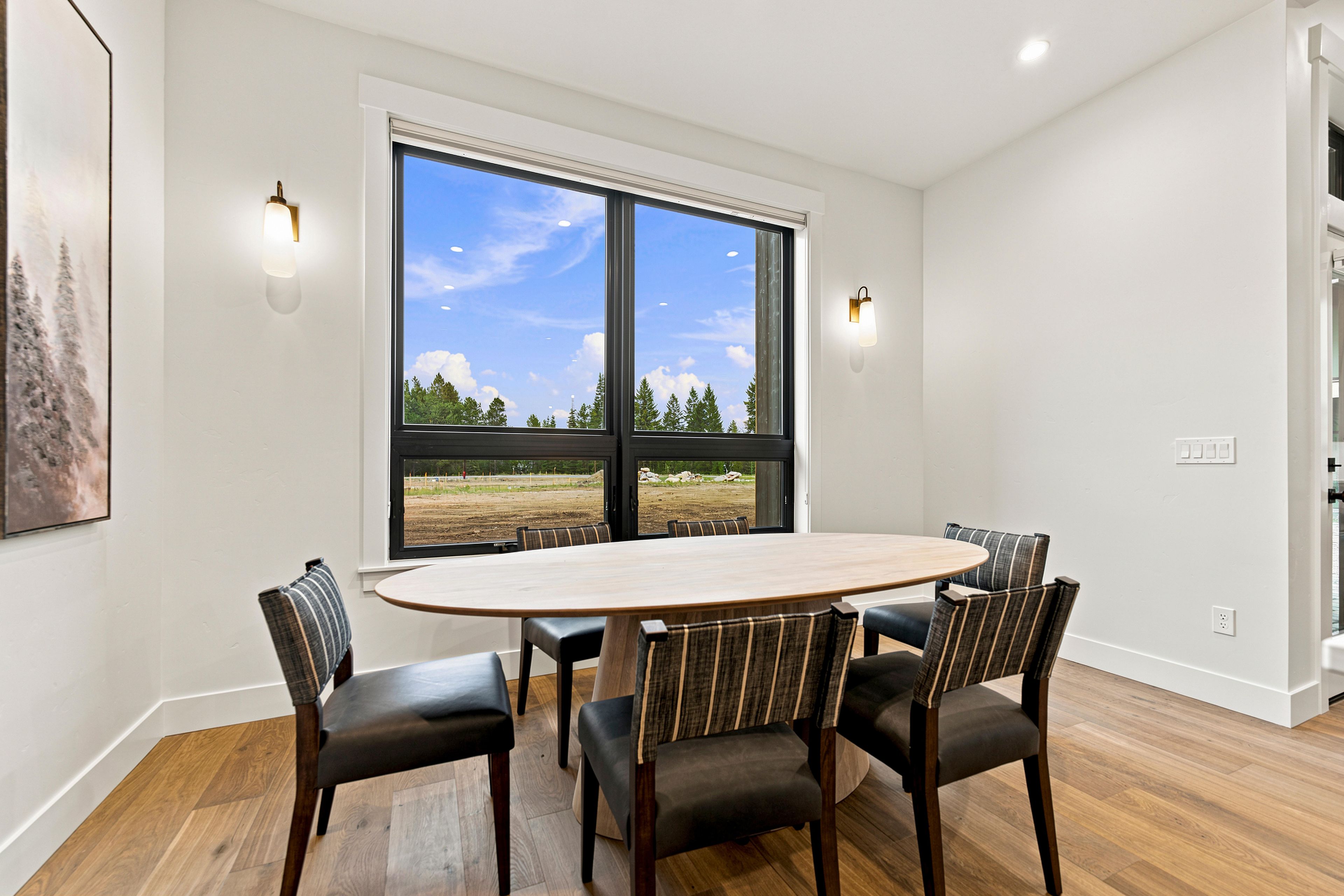 A dining area with a large oval table, four chairs, and two wall-mounted lights.