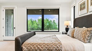 Ein Schlafzimmer mit großem Fenster, einem Bett mit gemusterten Betttextilien und einem Nachttisch mit Lampe.