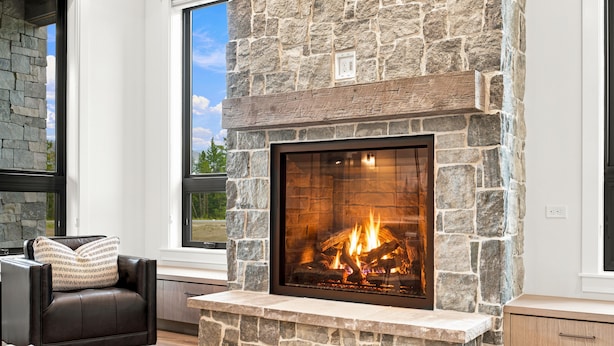 A stone fireplace with a fire, a leather sofa, and a view of the outdoors through a window.