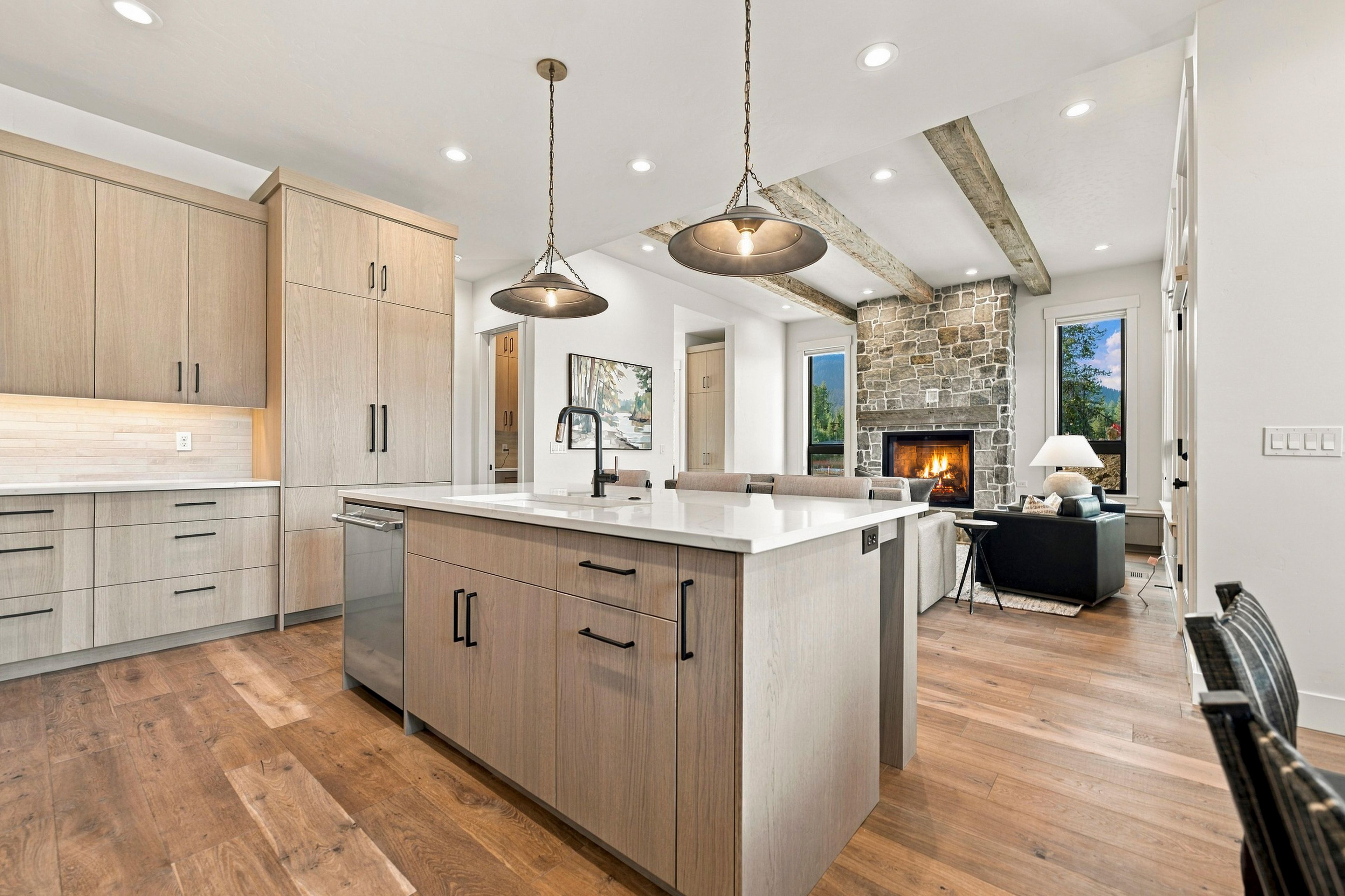 A spacious kitchen with wooden cabinets, a central island, pendant lighting, and a stone fireplace in the background.