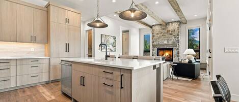 A spacious kitchen with wooden cabinets, a central island, pendant lighting, and a stone fireplace in the background.