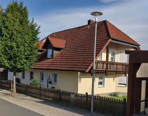 A two-story house with a red-tiled roof, a balcony, and a fenced yard.