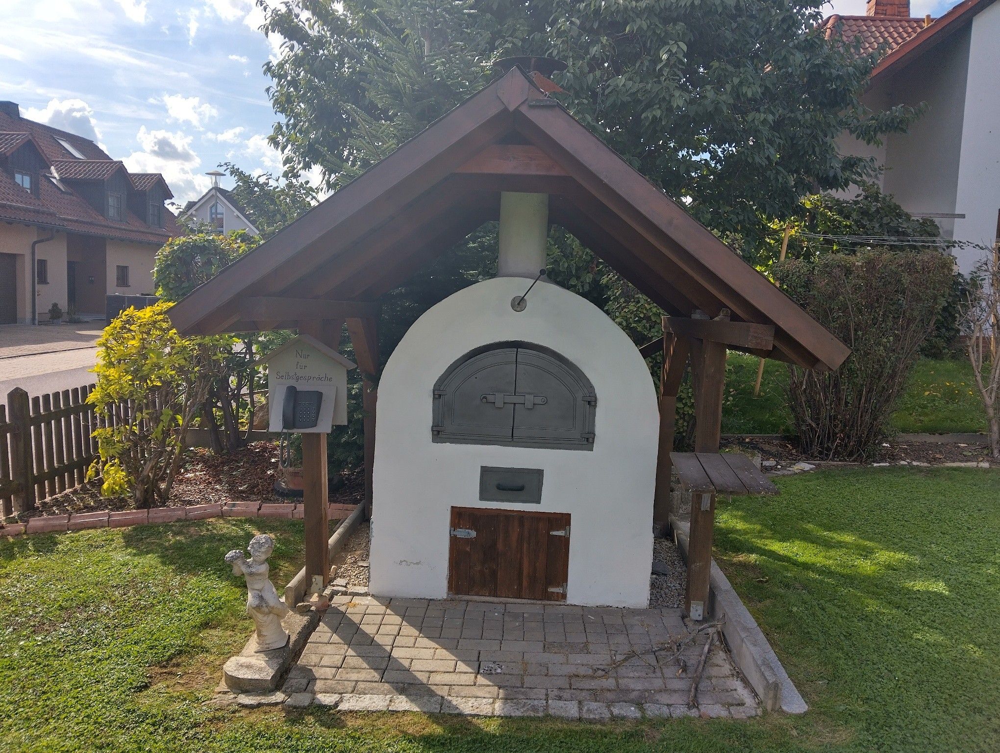 Una pequeña estructura blanca de arco con techo de madera, una puerta y un buzón.