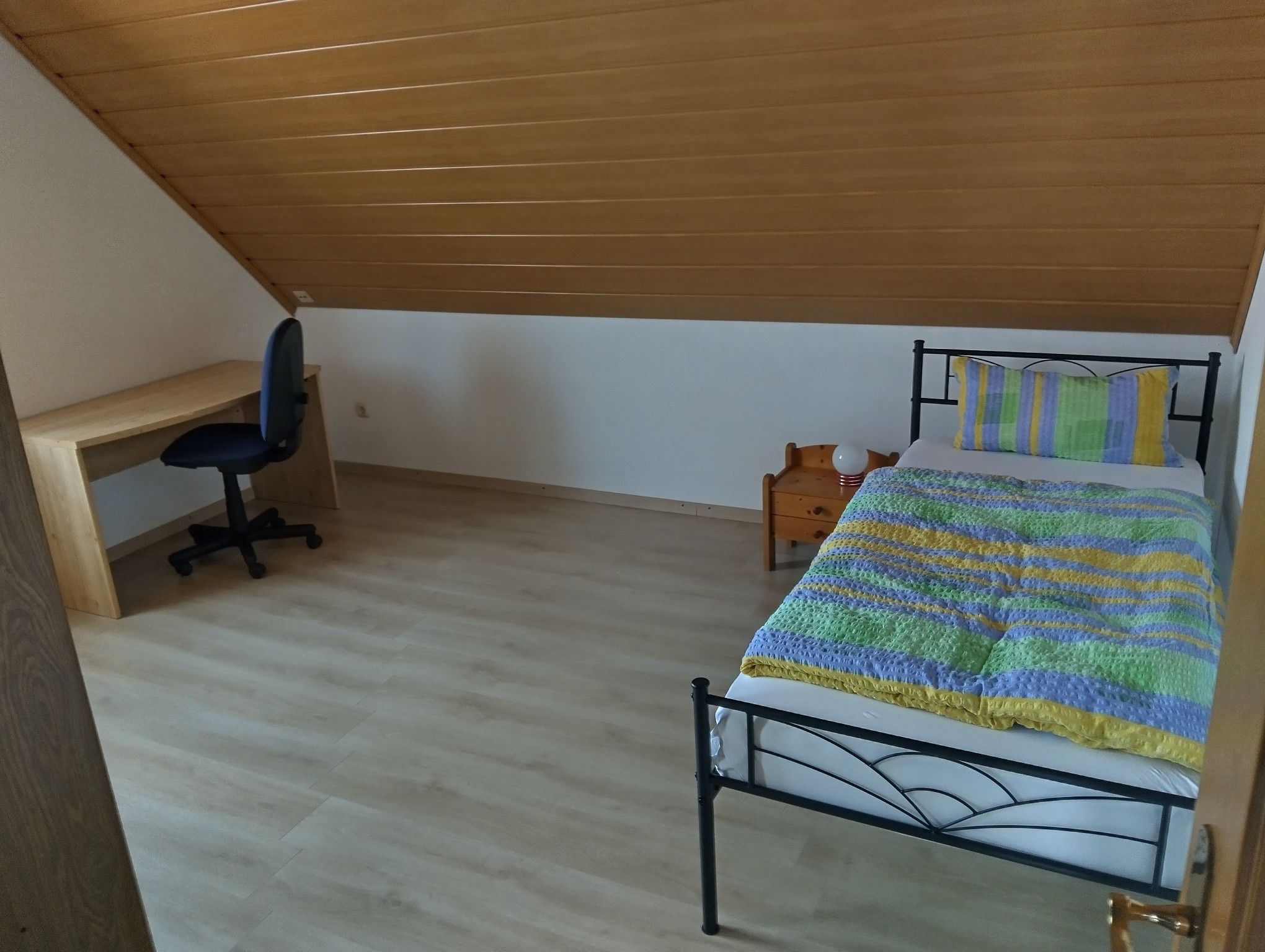 A bedroom with a bed, a desk, and a chair.