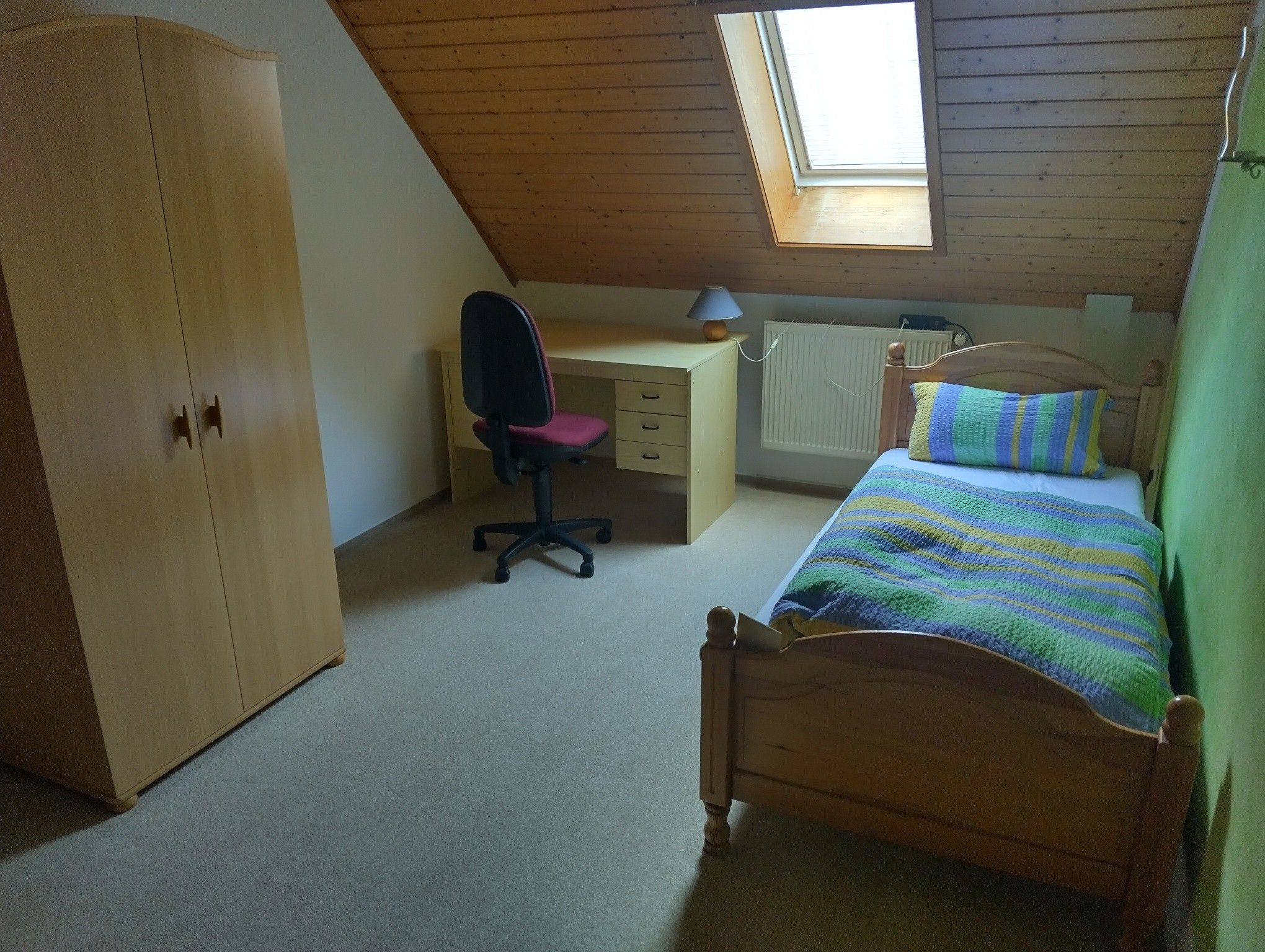 Une chambre avec un plafond en pente, un bureau, une chaise, un lit et une armoire.