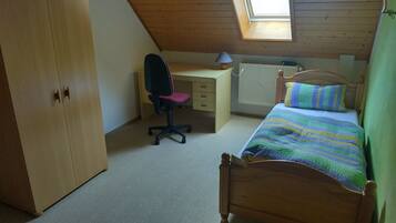 Une chambre avec un plafond en pente, un bureau, une chaise, un lit et une armoire.