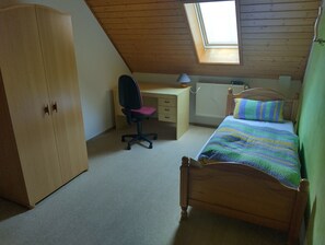 A bedroom with a sloped ceiling, a desk, a chair, a bed, and a wardrobe.